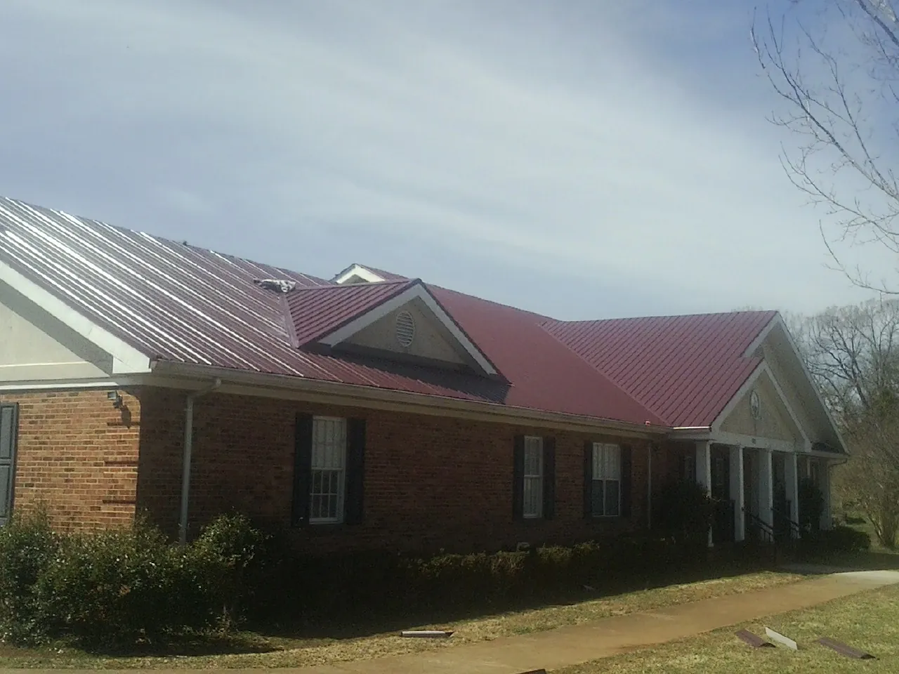 Red metal roof with gabled entries on a long brick building, from a Hail Damage Roof Repair job in Chesapeake City
