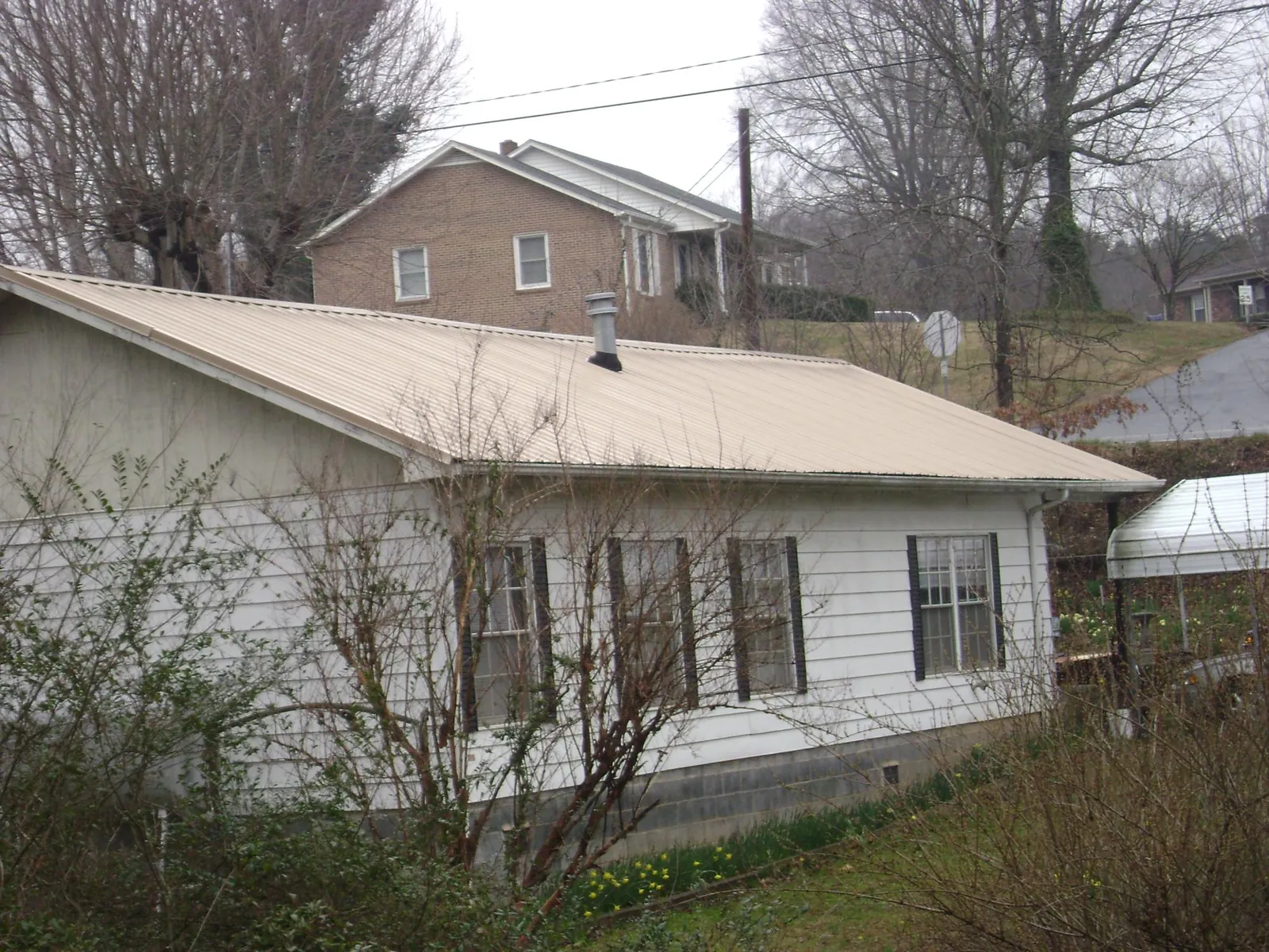 Tan metal roof on a white sided house set into a hillside — Commercial Roofing by Roofing Brothers in Chesapeake City
